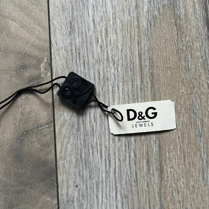 Dolce & Gabbana X Dog Tag Necklace (DJ0911) is a silver-tone necklace featuring a layered pendant with an almost square shape. The pendant is constructed from three layers: the front and back are X-shaped silver-tone plates with an engraved D&G logo at the center and visible screws at each corner, while the middle layer is a flat black square insert. The necklace is finished with a silver-tone paperclip-style chain.