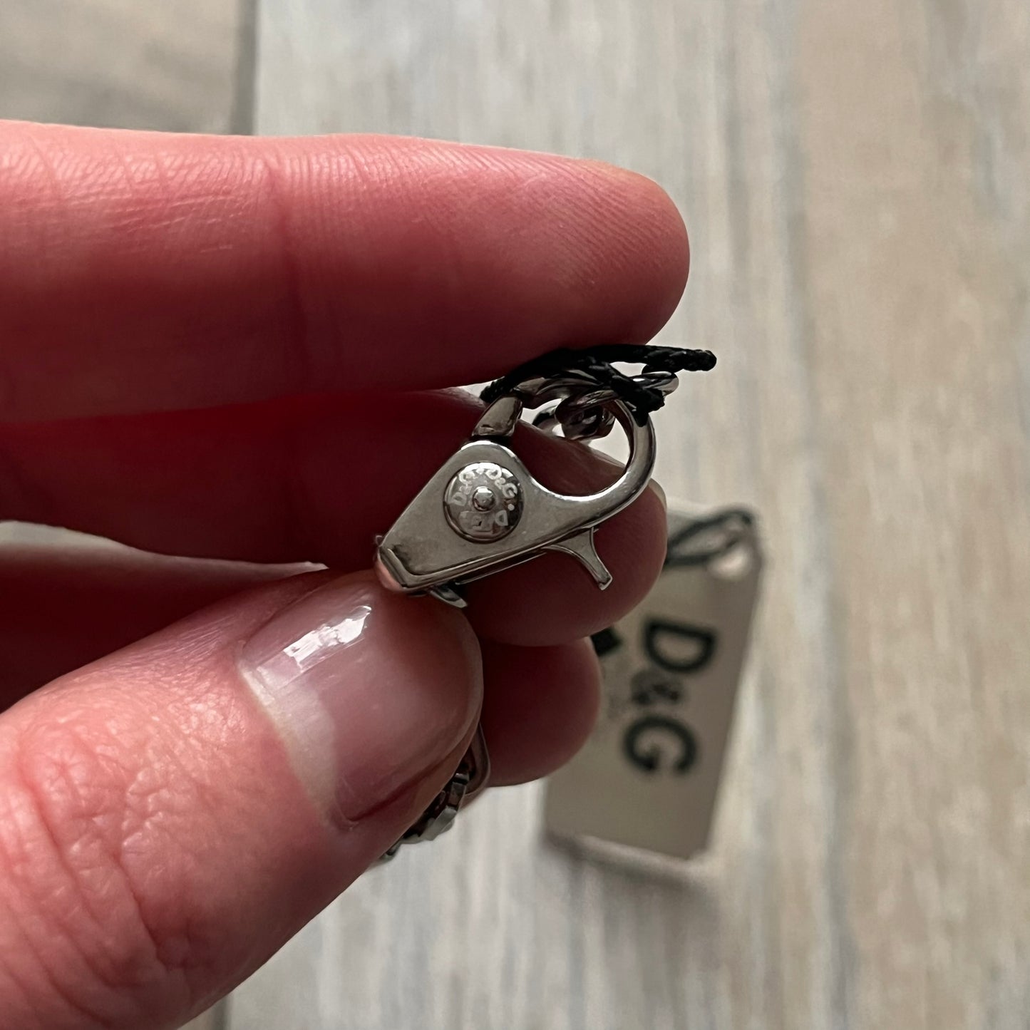 Dolce & Gabbana X Dog Tag Necklace (DJ0911) is a silver-tone necklace featuring a layered pendant with an almost square shape. The pendant is constructed from three layers: the front and back are X-shaped silver-tone plates with an engraved D&G logo at the center and visible screws at each corner, while the middle layer is a flat black square insert. The necklace is finished with a silver-tone paperclip-style chain.