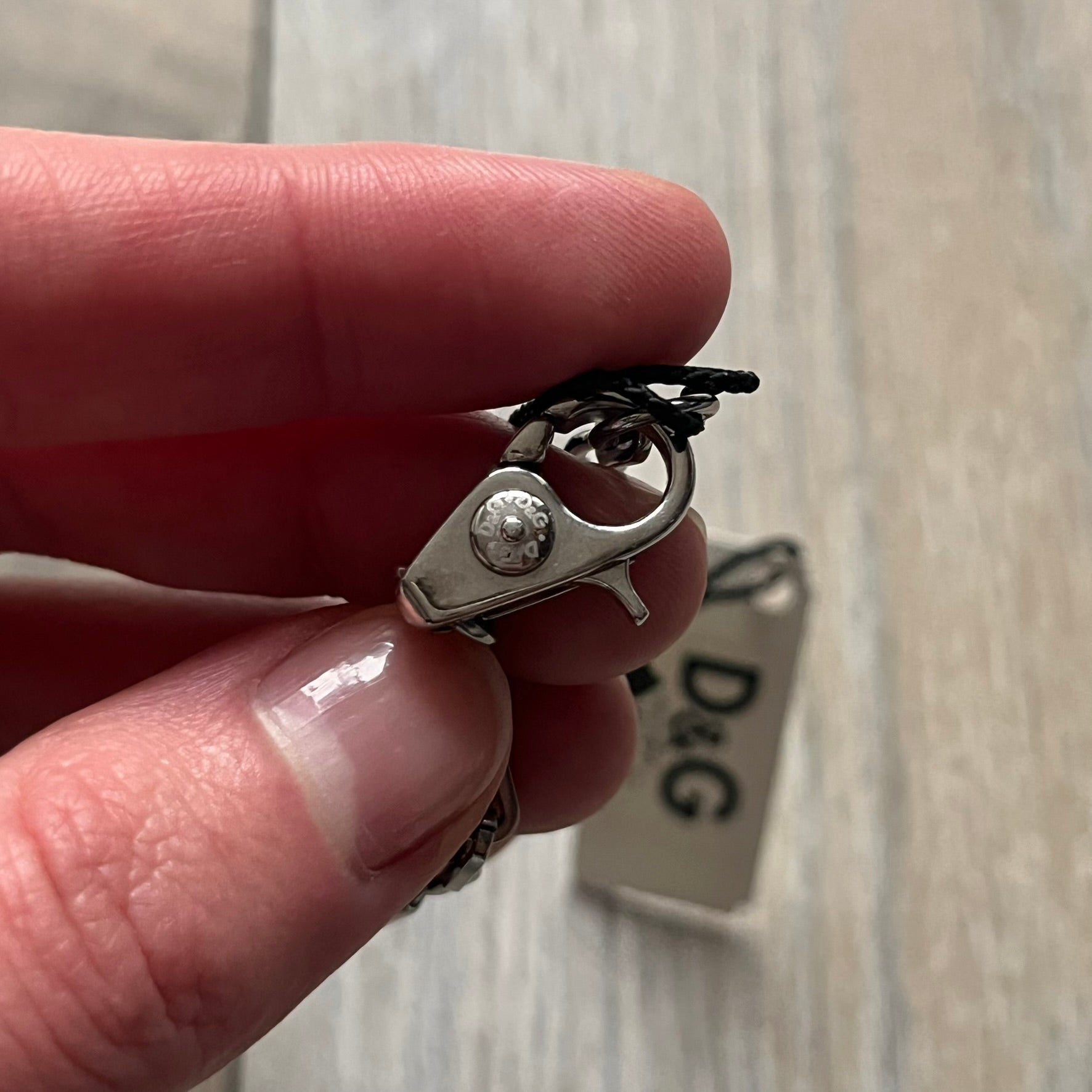Dolce & Gabbana X Dog Tag Necklace (DJ0911) is a silver-tone necklace featuring a layered pendant with an almost square shape. The pendant is constructed from three layers: the front and back are X-shaped silver-tone plates with an engraved D&G logo at the center and visible screws at each corner, while the middle layer is a flat black square insert. The necklace is finished with a silver-tone paperclip-style chain.