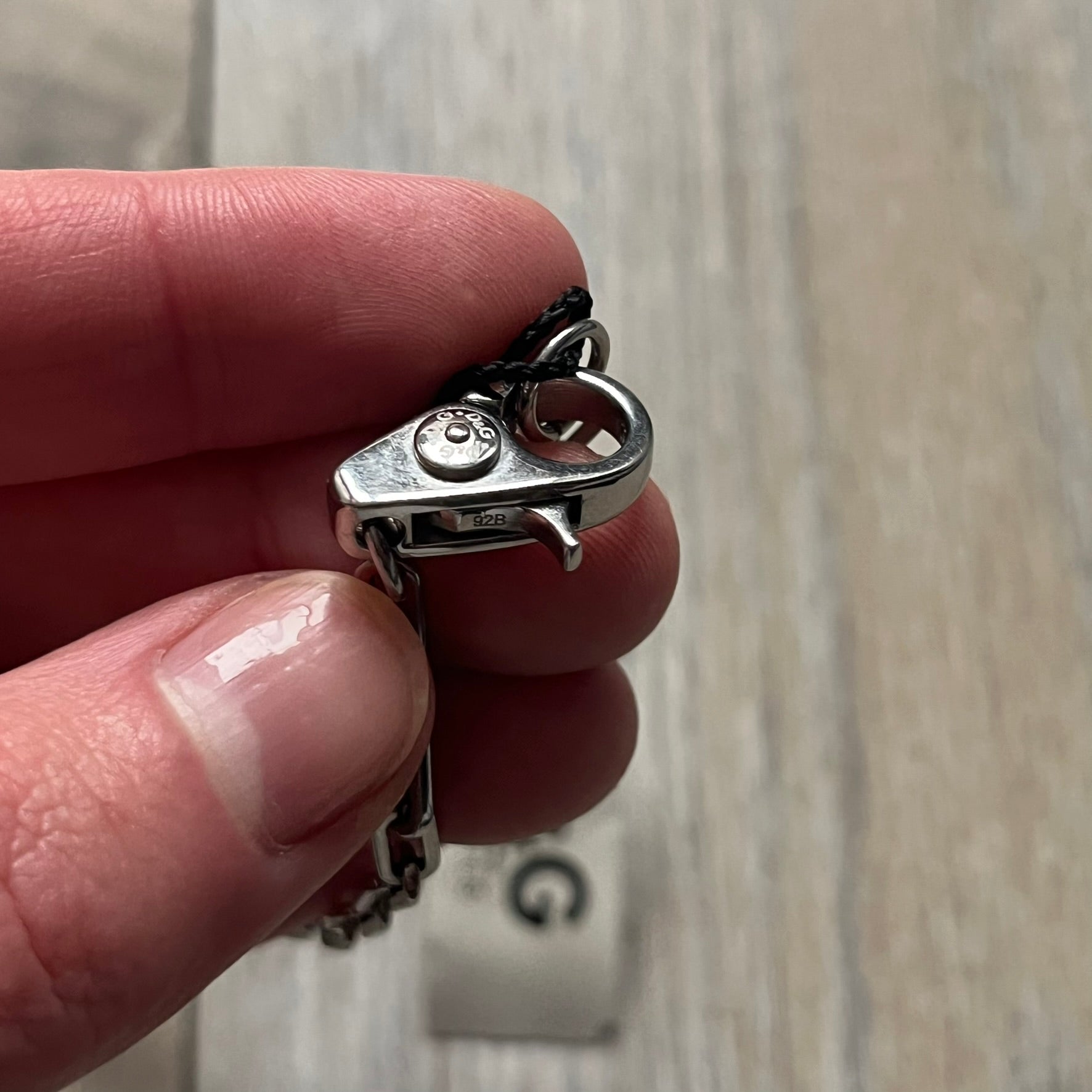 Dolce & Gabbana X Dog Tag Necklace (DJ0911) is a silver-tone necklace featuring a layered pendant with an almost square shape. The pendant is constructed from three layers: the front and back are X-shaped silver-tone plates with an engraved D&G logo at the center and visible screws at each corner, while the middle layer is a flat black square insert. The necklace is finished with a silver-tone paperclip-style chain.