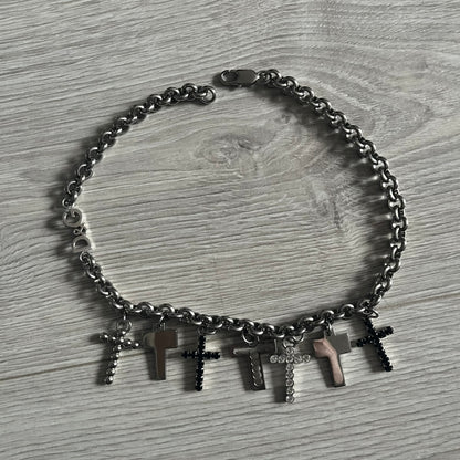 Dolce & Gabbana 7 Crosses Stainless Steel Choker Necklace. Crafted from polished stainless steel, this necklace features seven dangling crosses in varying designs, including full metal, black stones, white stones, and cut-out styles. One section of the chain incorporates a D&G logo in place of links. Comes with original box and dustbag.
