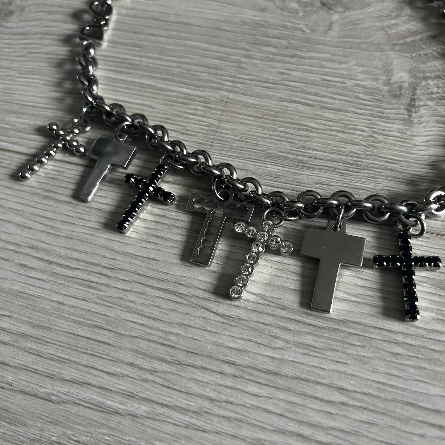 Dolce & Gabbana 7 Crosses Stainless Steel Choker Necklace. Crafted from polished stainless steel, this necklace features seven dangling crosses in varying designs, including full metal, black stones, white stones, and cut-out styles. One section of the chain incorporates a D&G logo in place of links. Comes with original box and dustbag.