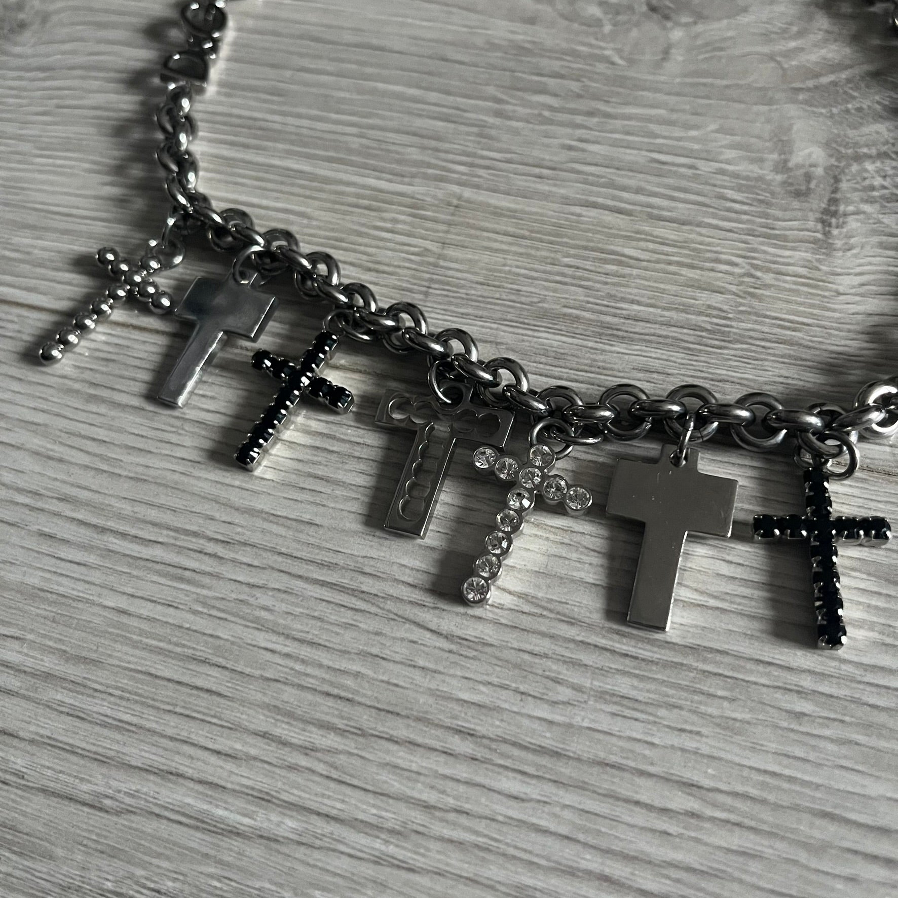Dolce & Gabbana 7 Crosses Stainless Steel Choker Necklace. Crafted from polished stainless steel, this necklace features seven dangling crosses in varying designs, including full metal, black stones, white stones, and cut-out styles. One section of the chain incorporates a D&G logo in place of links. Comes with original box and dustbag.