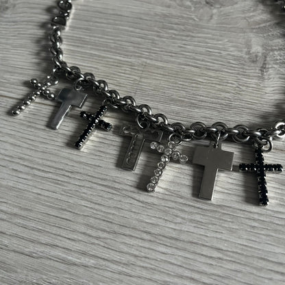 Dolce & Gabbana 7 Crosses Stainless Steel Choker Necklace. Crafted from polished stainless steel, this necklace features seven dangling crosses in varying designs, including full metal, black stones, white stones, and cut-out styles. One section of the chain incorporates a D&G logo in place of links. Comes with original box and dustbag.