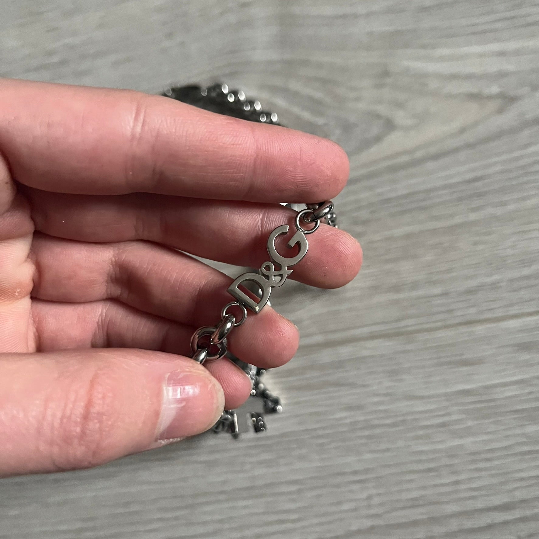 Dolce & Gabbana 7 Crosses Stainless Steel Choker Necklace. Crafted from polished stainless steel, this necklace features seven dangling crosses in varying designs, including full metal, black stones, white stones, and cut-out styles. One section of the chain incorporates a D&G logo in place of links. Comes with original box and dustbag.