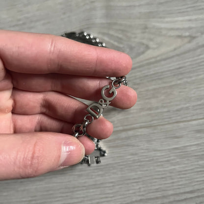 Dolce & Gabbana 7 Crosses Stainless Steel Choker Necklace. Crafted from polished stainless steel, this necklace features seven dangling crosses in varying designs, including full metal, black stones, white stones, and cut-out styles. One section of the chain incorporates a D&G logo in place of links. Comes with original box and dustbag.