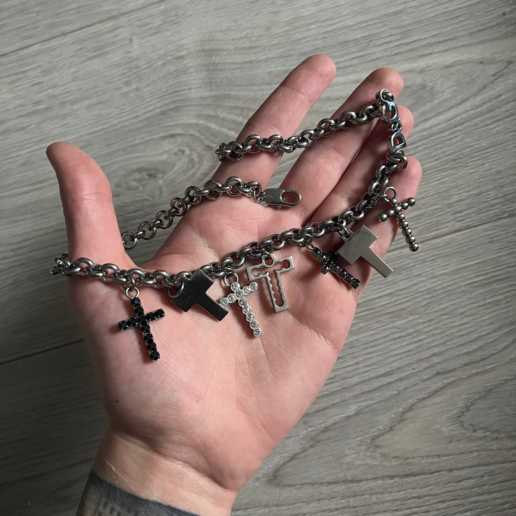 Dolce & Gabbana 7 Crosses Stainless Steel Choker Necklace. Crafted from polished stainless steel, this necklace features seven dangling crosses in varying designs, including full metal, black stones, white stones, and cut-out styles. One section of the chain incorporates a D&G logo in place of links. Comes with original box and dustbag.