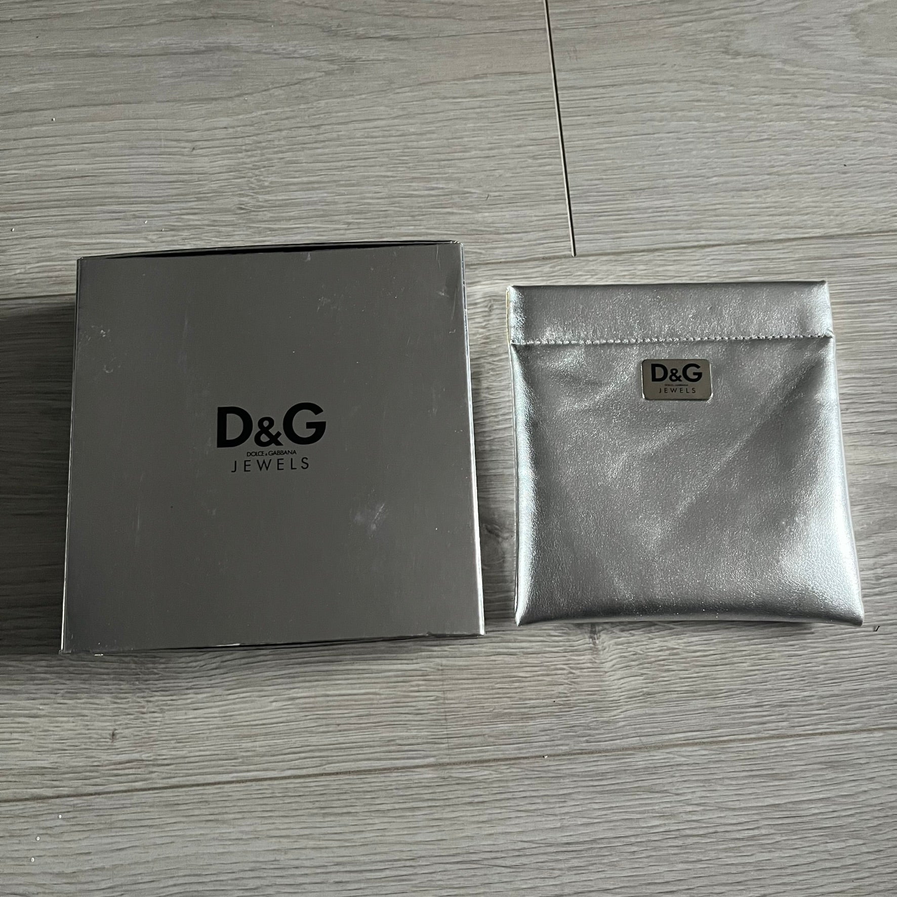 Dolce & Gabbana 7 Crosses Stainless Steel Choker Necklace. Crafted from polished stainless steel, this necklace features seven dangling crosses in varying designs, including full metal, black stones, white stones, and cut-out styles. One section of the chain incorporates a D&G logo in place of links. Comes with original box and dustbag.