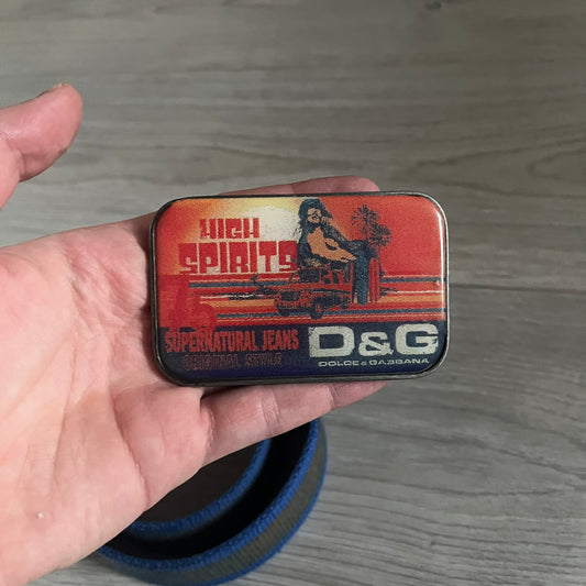 Dolce &amp; Gabbana “High Spirits” Fabric Belt in blue with a brown/gray central stripe and enamel-finished metal buckle. The buckle features vintage iconography and “High Spirits” lettering in vivid orange/red and navy tones. A rare 2000s-era Dolce &amp; Gabbana belt showcasing the brand’s early denim aesthetic.