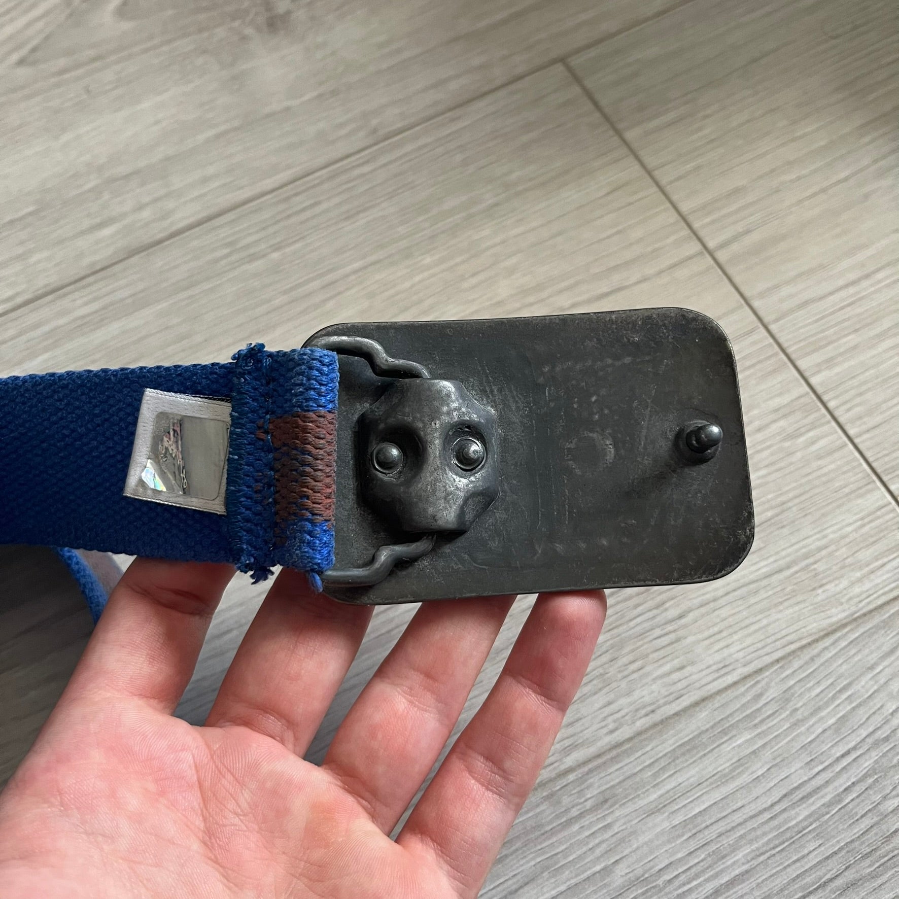 Dolce &amp; Gabbana “High Spirits” Fabric Belt in blue with a brown central stripe and enamel-finished metal buckle. The buckle features vintage iconography and “High Spirits” lettering in vivid orange/red and navy tones. A rare 2000s-era Dolce &amp; Gabbana belt showcasing the brand’s early denim aesthetic.