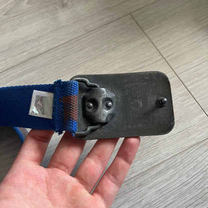 Dolce &amp; Gabbana “High Spirits” Fabric Belt in blue with a brown central stripe and enamel-finished metal buckle. The buckle features vintage iconography and “High Spirits” lettering in vivid orange/red and navy tones. A rare 2000s-era Dolce &amp; Gabbana belt showcasing the brand’s early denim aesthetic.