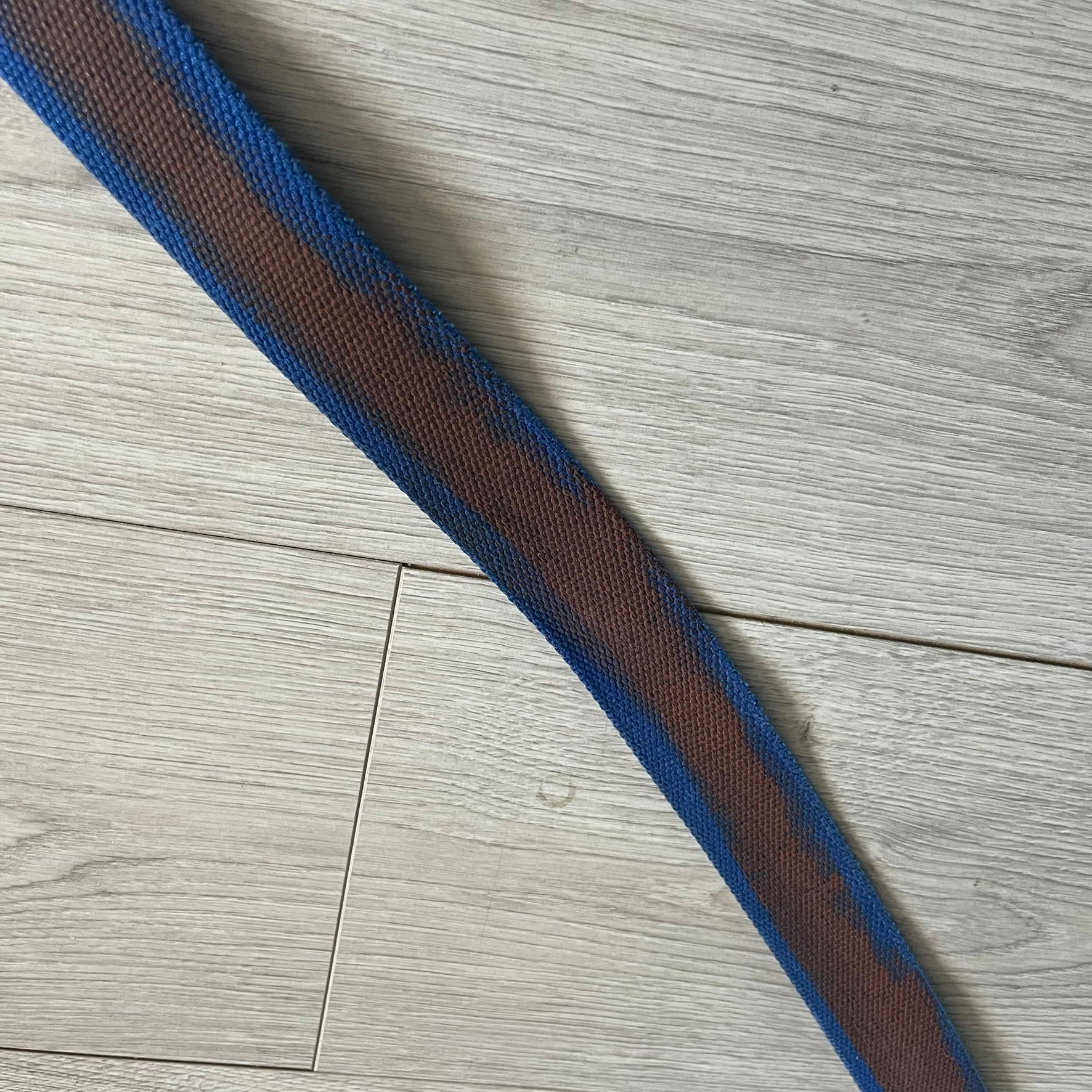 Dolce &amp; Gabbana “High Spirits” Fabric Belt in blue with a brown central stripe and enamel-finished metal buckle. The buckle features vintage iconography and “High Spirits” lettering in vivid orange/red and navy tones. A rare 2000s-era Dolce &amp; Gabbana belt showcasing the brand’s early denim aesthetic.