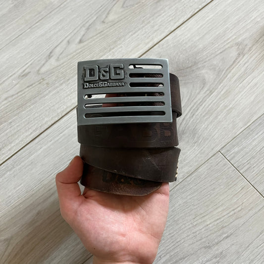 Dolce &amp; Gabbana USA Flag Leather Belt crafted from brown leather with concave, sunken Dolce &amp; Gabbana and D&amp;G text detailing along the strap. The metal buckle is designed in a flag-inspired layout, featuring six horizontal cut-out lines and D&amp;G Dolce &amp; Gabbana text in the upper-left corner in place of traditional stars. The belt shows visible wear consistent with age, giving it a heavily worn, vintage finish.