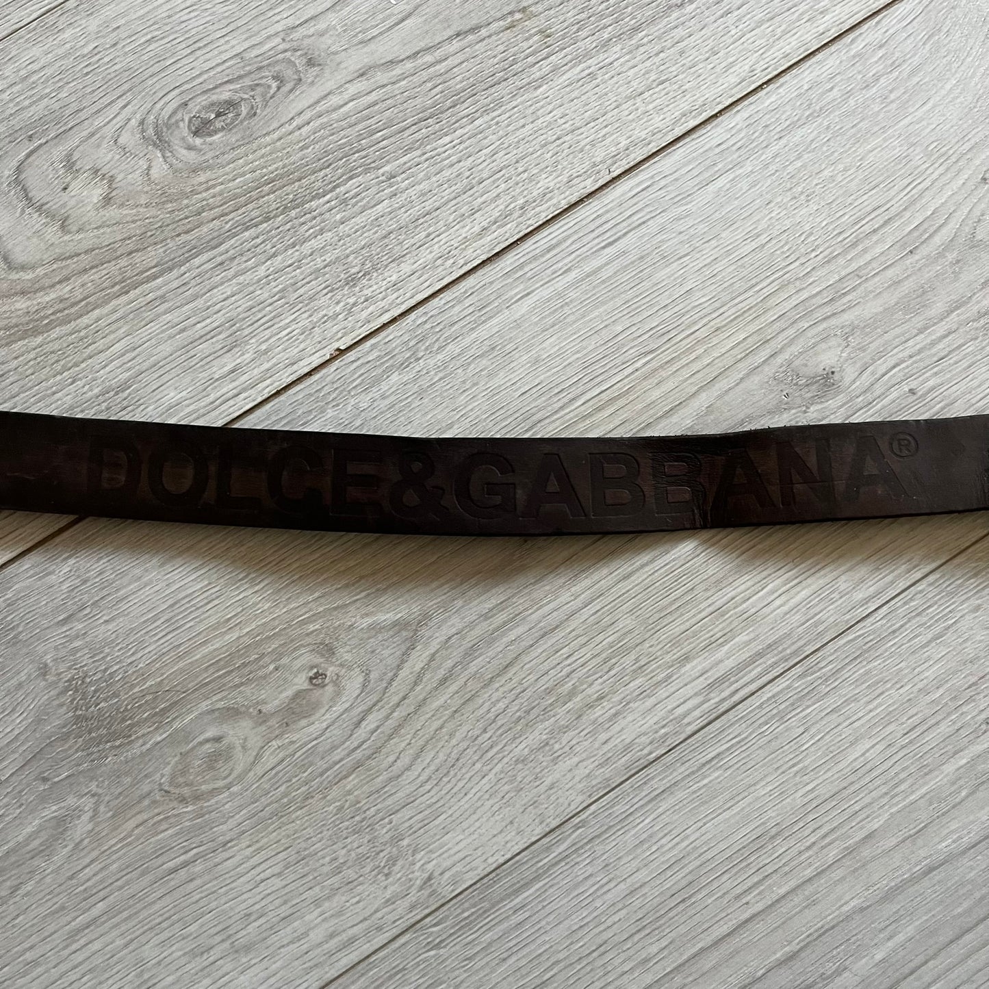 Dolce &amp; Gabbana USA Flag Leather Belt crafted from brown leather with concave, sunken Dolce &amp; Gabbana and D&amp;G text detailing along the strap. The metal buckle is designed in a flag-inspired layout, featuring six horizontal cut-out lines and D&amp;G Dolce &amp; Gabbana text in the upper-left corner in place of traditional stars. The belt shows visible wear consistent with age, giving it a heavily worn, vintage finish.