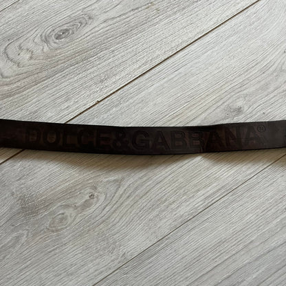 Dolce &amp; Gabbana USA Flag Leather Belt crafted from brown leather with concave, sunken Dolce &amp; Gabbana and D&amp;G text detailing along the strap. The metal buckle is designed in a flag-inspired layout, featuring six horizontal cut-out lines and D&amp;G Dolce &amp; Gabbana text in the upper-left corner in place of traditional stars. The belt shows visible wear consistent with age, giving it a heavily worn, vintage finish.