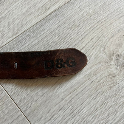 Dolce &amp; Gabbana USA Flag Leather Belt crafted from brown leather with concave, sunken Dolce &amp; Gabbana and D&amp;G text detailing along the strap. The metal buckle is designed in a flag-inspired layout, featuring six horizontal cut-out lines and D&amp;G Dolce &amp; Gabbana text in the upper-left corner in place of traditional stars. The belt shows visible wear consistent with age, giving it a heavily worn, vintage finish.
