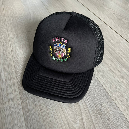 Drake Anita Max Wynn Pink Trucker Hat in all-black front panel, sides and cap, featuring a collection of graphics including a woman with an oversized head, two yellow dollar signs, and “ANITA” in pink, “MAX” in blue, and “WYNN” in green. Designed with a mesh back for breathability, a snapback closure for adjustability, and polyester construction to keep the head cool. A playful tribute to Drake’s alter ego and love of g4mbling.