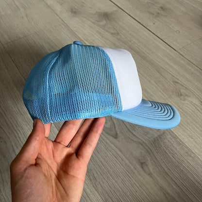 Drake Anita Max Wynn Pink Trucker Hat with a white front panel and baby blue sides and cap, featuring a collection of graphics including a woman with an oversized head, two yellow dollar signs, and “ANITA” in pink, “MAX” in blue, and “WYNN” in green. Designed with a mesh back for breathability, a snapback closure for adjustability, and polyester construction to keep the head cool. A playful tribute to Drake’s alter ego and love of g4mbling.