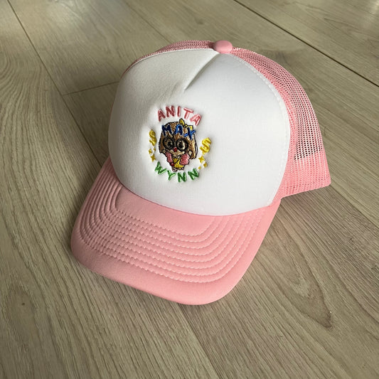 The Drake Anita Max Wynn Hat Punk is a trucker hat that pays tribute to hip-hop artist Drake’s alter ego, Anita Max Wynn. Pink sides and cap, white front.
The hat was inspired by Drake’s love of gambling and his need to get a "max win." The details include a collection of graphics on the front, such as a woman with an oversized head and a pink jacket, two yellow dollar signs, "ANITA" in pink, "MAX" in Blue, and " WYNN" in green. The hat features an construction with a mesh back. A traditional snapback provi