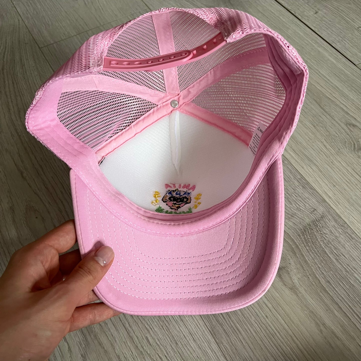 The Drake Anita Max Wynn Hat Punk is a trucker hat that pays tribute to hip-hop artist Drake’s alter ego, Anita Max Wynn. Pink sides and cap, white front.
The hat was inspired by Drake’s love of gambling and his need to get a "max win." The details include a collection of graphics on the front, such as a woman with an oversized head and a pink jacket, two yellow dollar signs, "ANITA" in pink, "MAX" in Blue, and " WYNN" in green. The hat features an construction with a mesh back. A traditional snapback provi