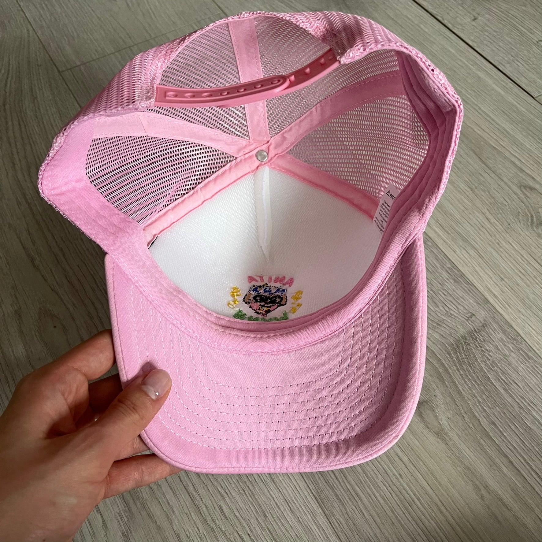 The Drake Anita Max Wynn Hat Punk is a trucker hat that pays tribute to hip-hop artist Drake’s alter ego, Anita Max Wynn. Pink sides and cap, white front.
The hat was inspired by Drake’s love of gambling and his need to get a "max win." The details include a collection of graphics on the front, such as a woman with an oversized head and a pink jacket, two yellow dollar signs, "ANITA" in pink, "MAX" in Blue, and " WYNN" in green. The hat features an construction with a mesh back. A traditional snapback provi