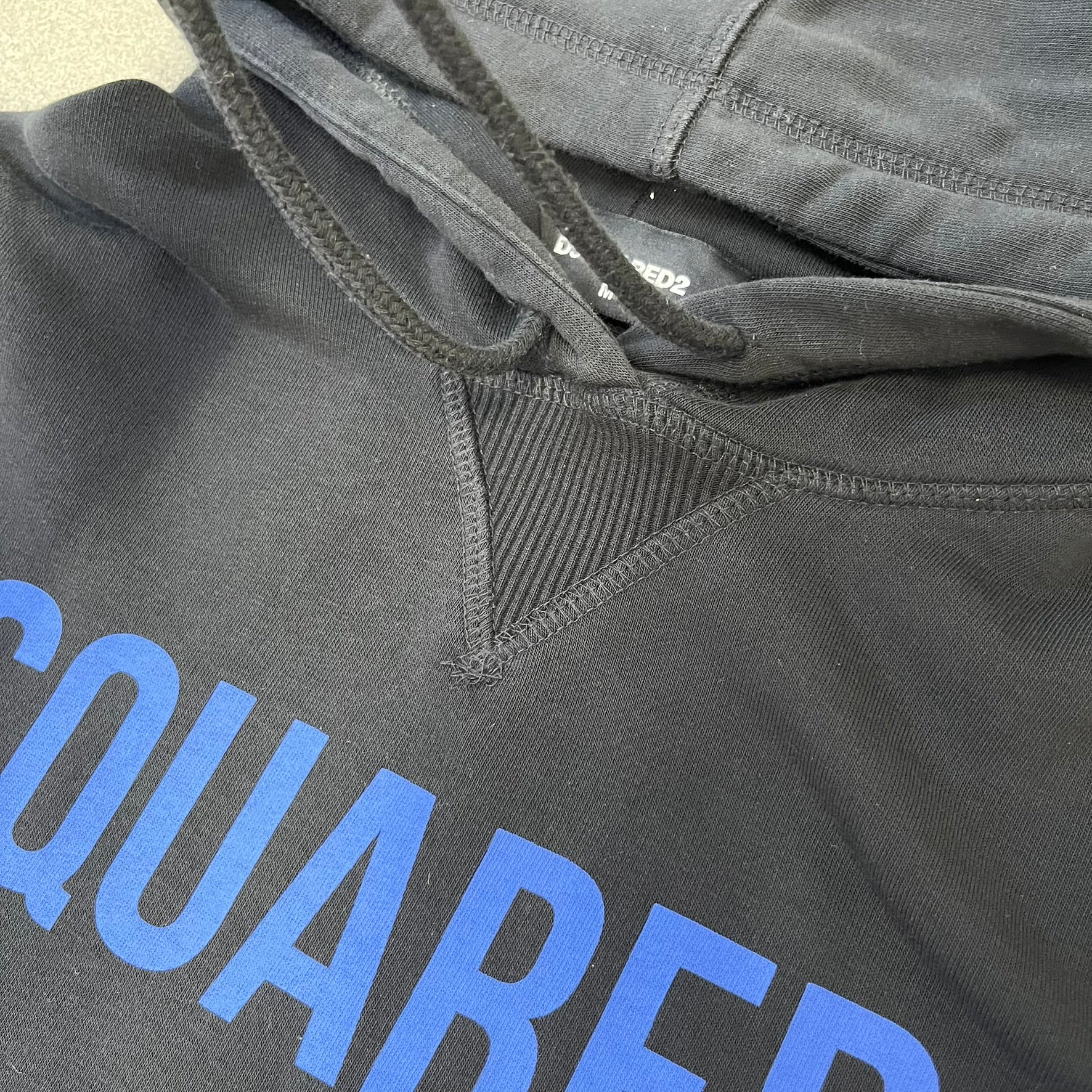 Dsquared2 2017 Western Cowboys Hoodie is a black hoodie featuring a blue Dsquared2 text logo across the upper front and a red square graphic on the lower right. Inside the square are two black cowboy figures wearing hats. The hoodie was made in Portugal.
