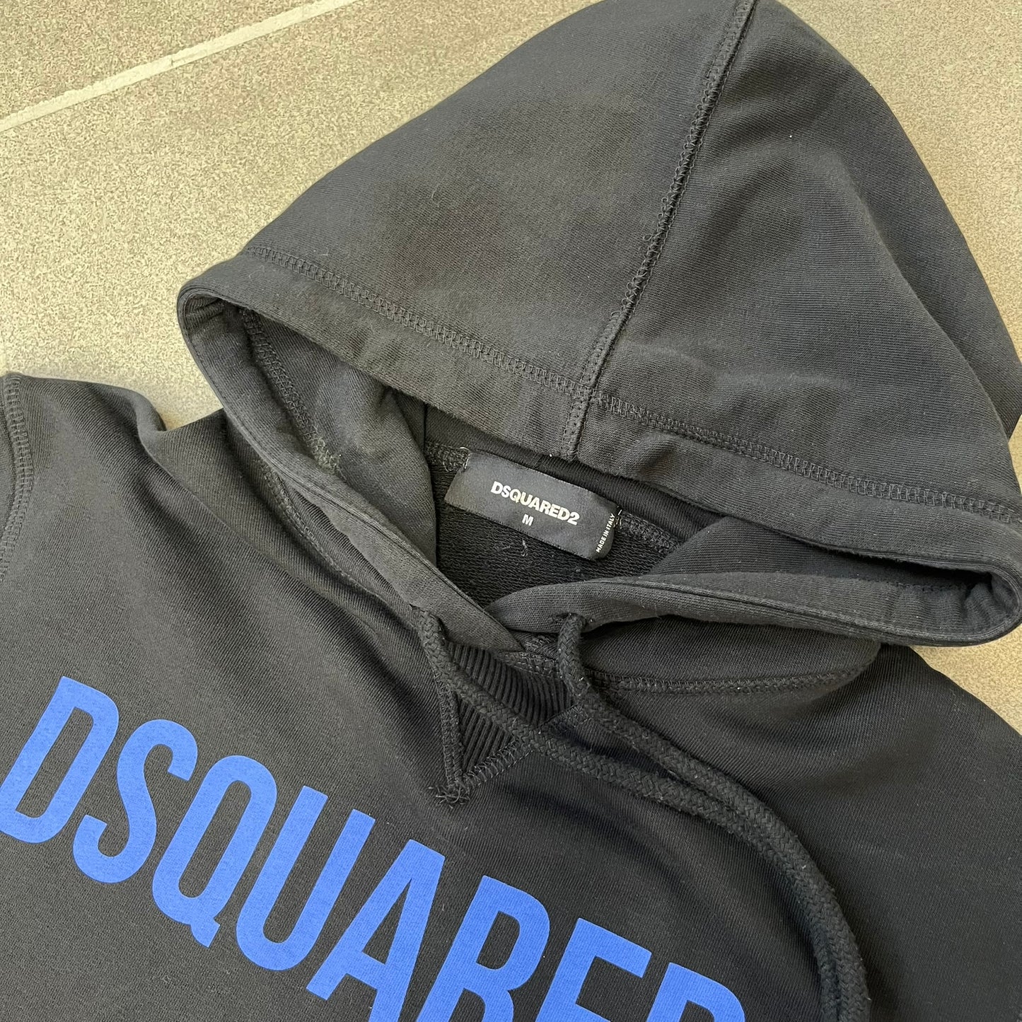Dsquared2 2017 Western Cowboys Hoodie is a black hoodie featuring a blue Dsquared2 text logo across the upper front and a red square graphic on the lower right. Inside the square are two black cowboy figures wearing hats. The hoodie was made in Portugal.
