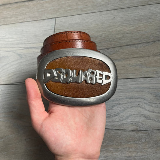 Dsquared2 Big Brown Hair Plaque Leather Belt is a leather belt featuring a large oval metal buckle with a silver-tone frame and brown short hair center. The buckle displays DSQUARED2 text in the middle, while the strap includes stamped branding and product details. Made from brown leather, the belt is size Medium.