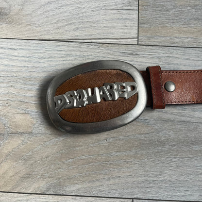 Dsquared2 Big Brown Hair Plaque Leather Belt is a leather belt featuring a large oval metal buckle with a silver-tone frame and brown short hair center. The buckle displays DSQUARED2 text in the middle, while the strap includes stamped branding and product details. Made from brown leather, the belt is size Medium.