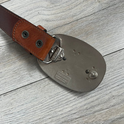 Dsquared2 Big Brown Hair Plaque Leather Belt is a leather belt featuring a large oval metal buckle with a silver-tone frame and brown short hair center. The buckle displays DSQUARED2 text in the middle, while the strap includes stamped branding and product details. Made from brown leather, the belt is size Medium.