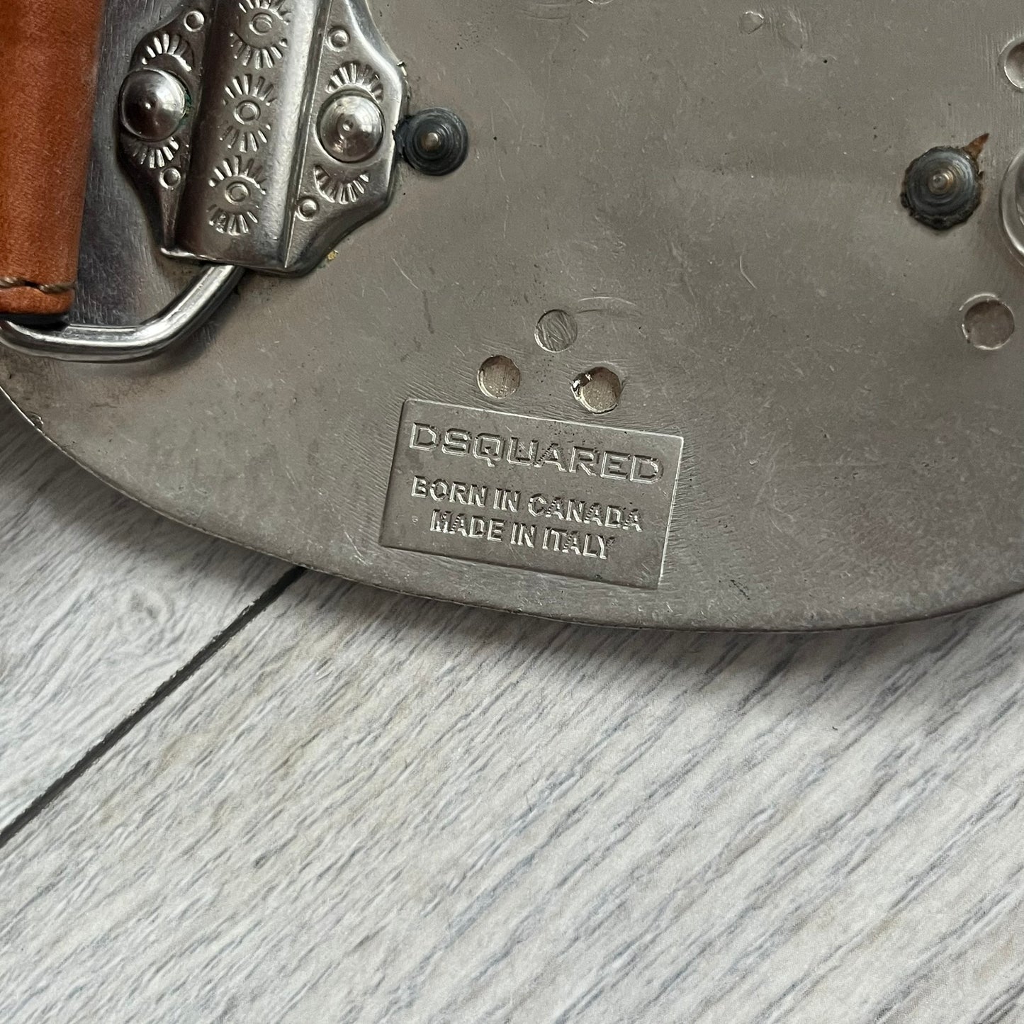 Dsquared2 Big Brown Hair Plaque Leather Belt is a leather belt featuring a large oval metal buckle with a silver-tone frame and brown short hair center. The buckle displays DSQUARED2 text in the middle, while the strap includes stamped branding and product details. Made from brown leather, the belt is size Medium.