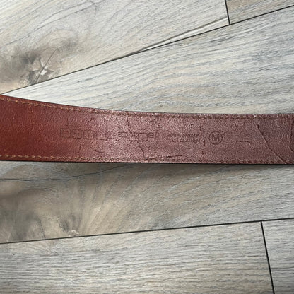 Dsquared2 Big Brown Hair Plaque Leather Belt is a leather belt featuring a large oval metal buckle with a silver-tone frame and brown short hair center. The buckle displays DSQUARED2 text in the middle, while the strap includes stamped branding and product details. Made from brown leather, the belt is size Medium.