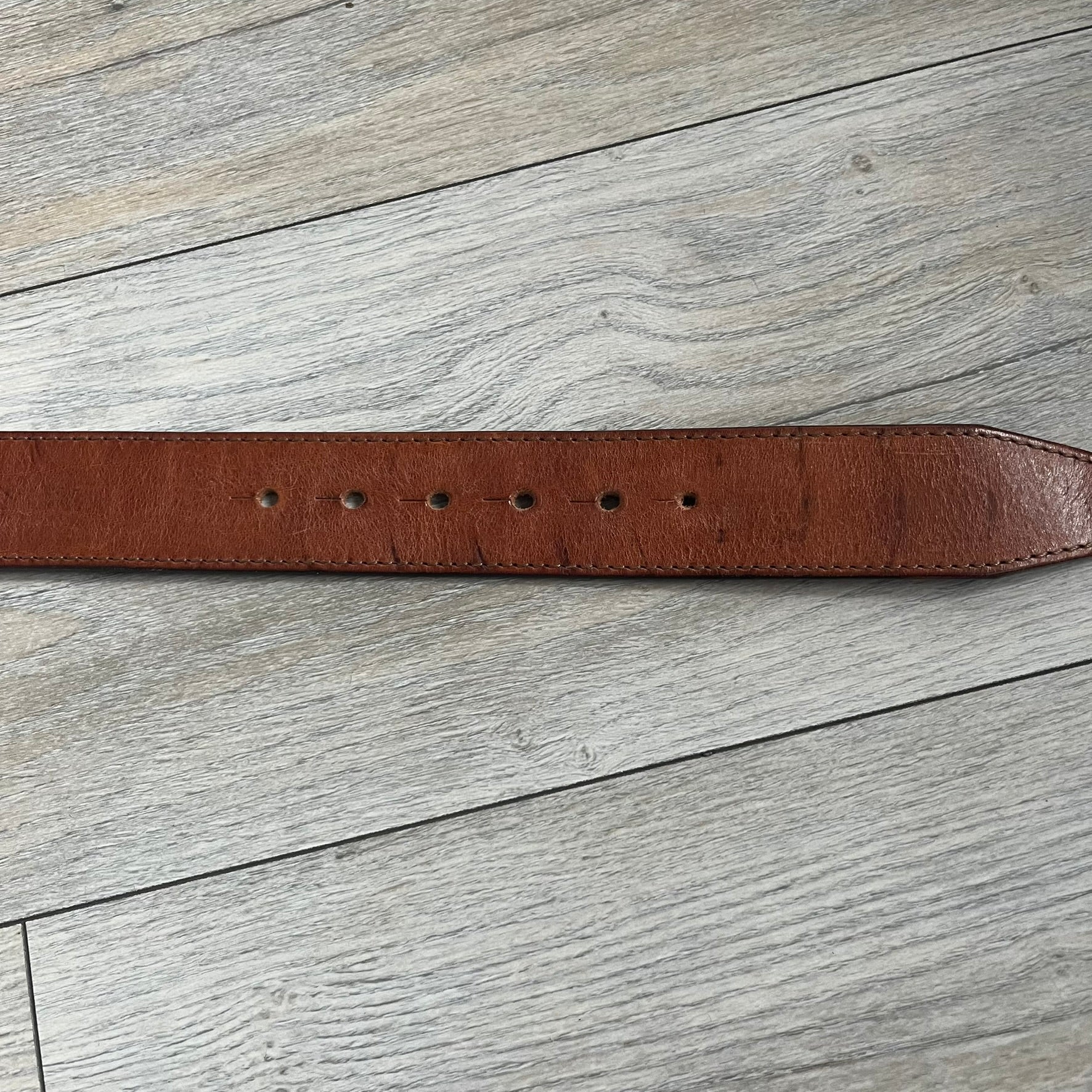 Dsquared2 Big Brown Hair Plaque Leather Belt is a leather belt featuring a large oval metal buckle with a silver-tone frame and brown short hair center. The buckle displays DSQUARED2 text in the middle, while the strap includes stamped branding and product details. Made from brown leather, the belt is size Medium.