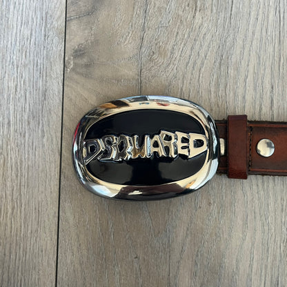 Dsquared2 Big Navy Plaque Leather Belt is a leather belt featuring a large oval metal buckle with a silver-tone frame and navy enamel center. The buckle displays DSQUARED2 text in the middle, while the strap includes stamped branding and product details. Made from brown leather, the belt is size small.