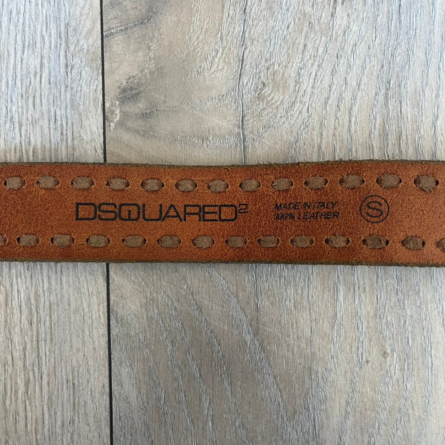 Dsquared2 Big Navy Plaque Leather Belt is a leather belt featuring a large oval metal buckle with a silver-tone frame and navy enamel center. The buckle displays DSQUARED2 text in the middle, while the strap includes stamped branding and product details. Made from brown leather, the belt is size small.