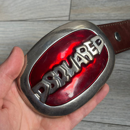 Dsquared2 Big Red Plaque Leather Belt is a leather belt featuring a large oval metal buckle with a silver-tone frame and red metallic center. The buckle displays DSQUARED2 text in the middle, while the strap includes stamped branding and product details. Made from brown leather, the belt is size small.
