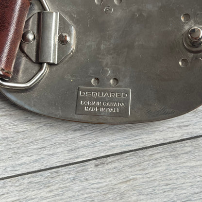 Dsquared2 Big Red Plaque Leather Belt is a leather belt featuring a large oval metal buckle with a silver-tone frame and red metallic center. The buckle displays DSQUARED2 text in the middle, while the strap includes stamped branding and product details. Made from brown leather, the belt is size small.