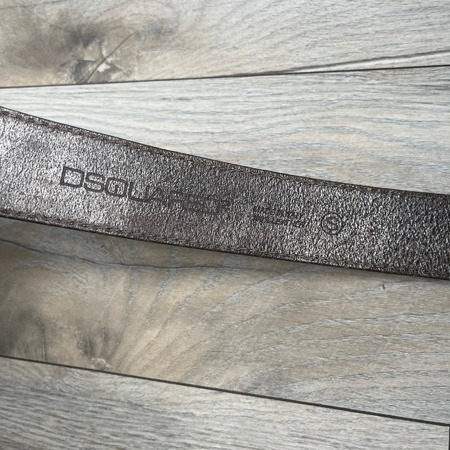 Dsquared2 Big Red Plaque Leather Belt is a leather belt featuring a large oval metal buckle with a silver-tone frame and red metallic center. The buckle displays DSQUARED2 text in the middle, while the strap includes stamped branding and product details. Made from brown leather, the belt is size small.