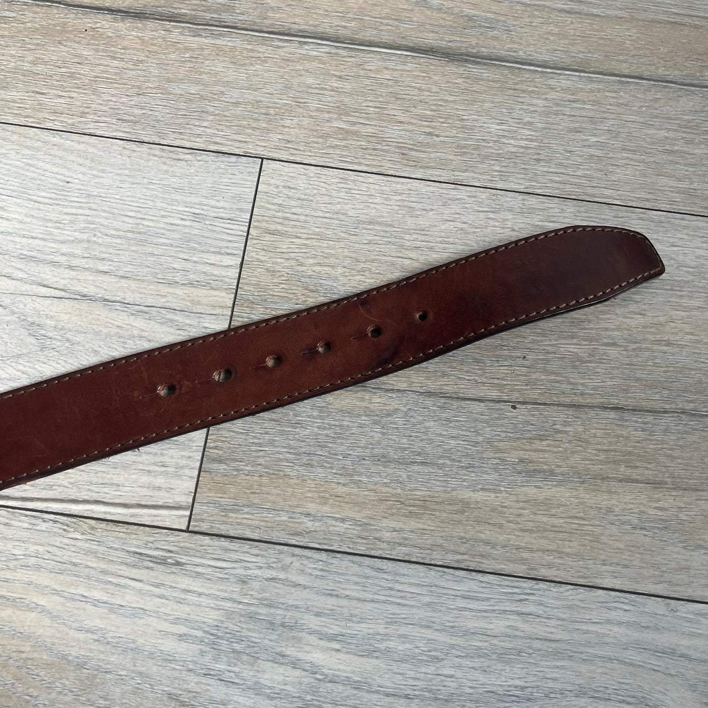 Dsquared2 Big Red Plaque Leather Belt is a leather belt featuring a large oval metal buckle with a silver-tone frame and red metallic center. The buckle displays DSQUARED2 text in the middle, while the strap includes stamped branding and product details. Made from brown leather, the belt is size small.