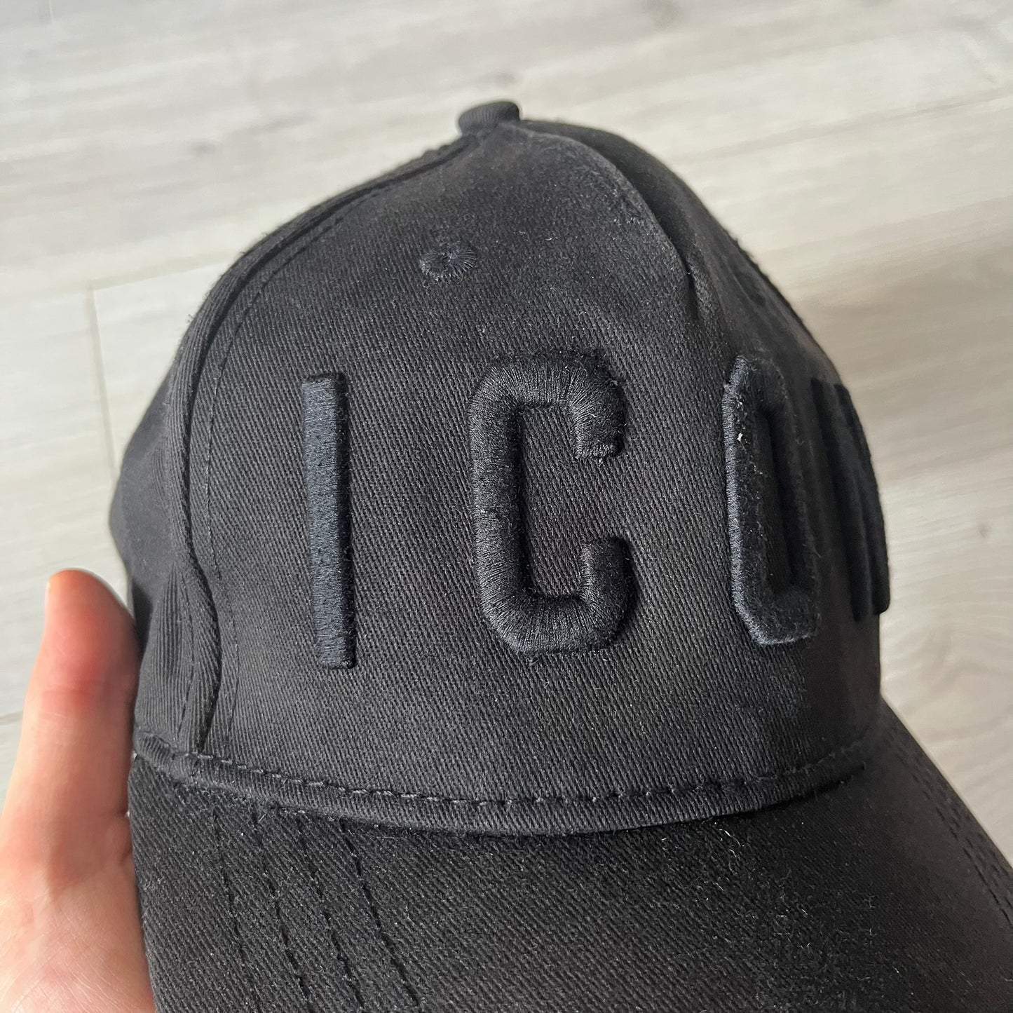 Black cap with 'IC' logo held by a hand on a light gray background