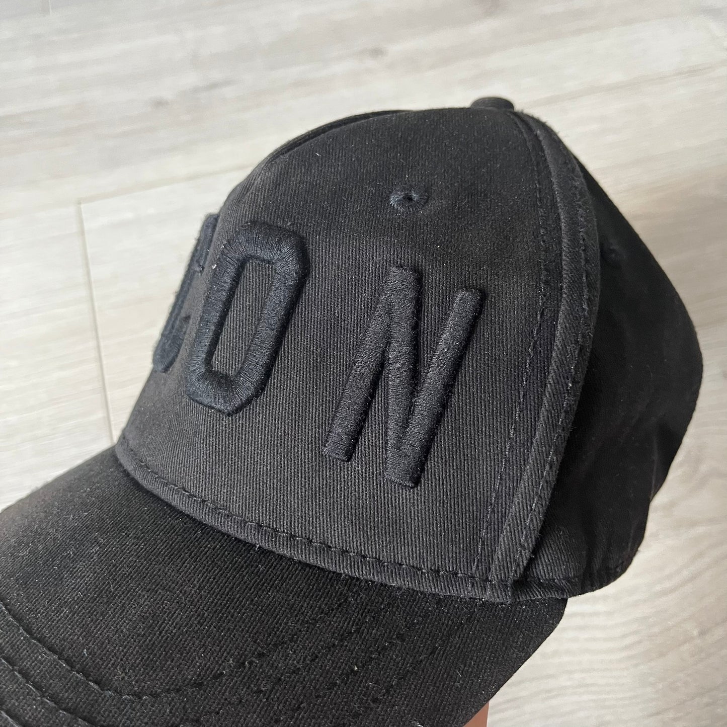 Black cap with 'DON' text on a light wooden surface