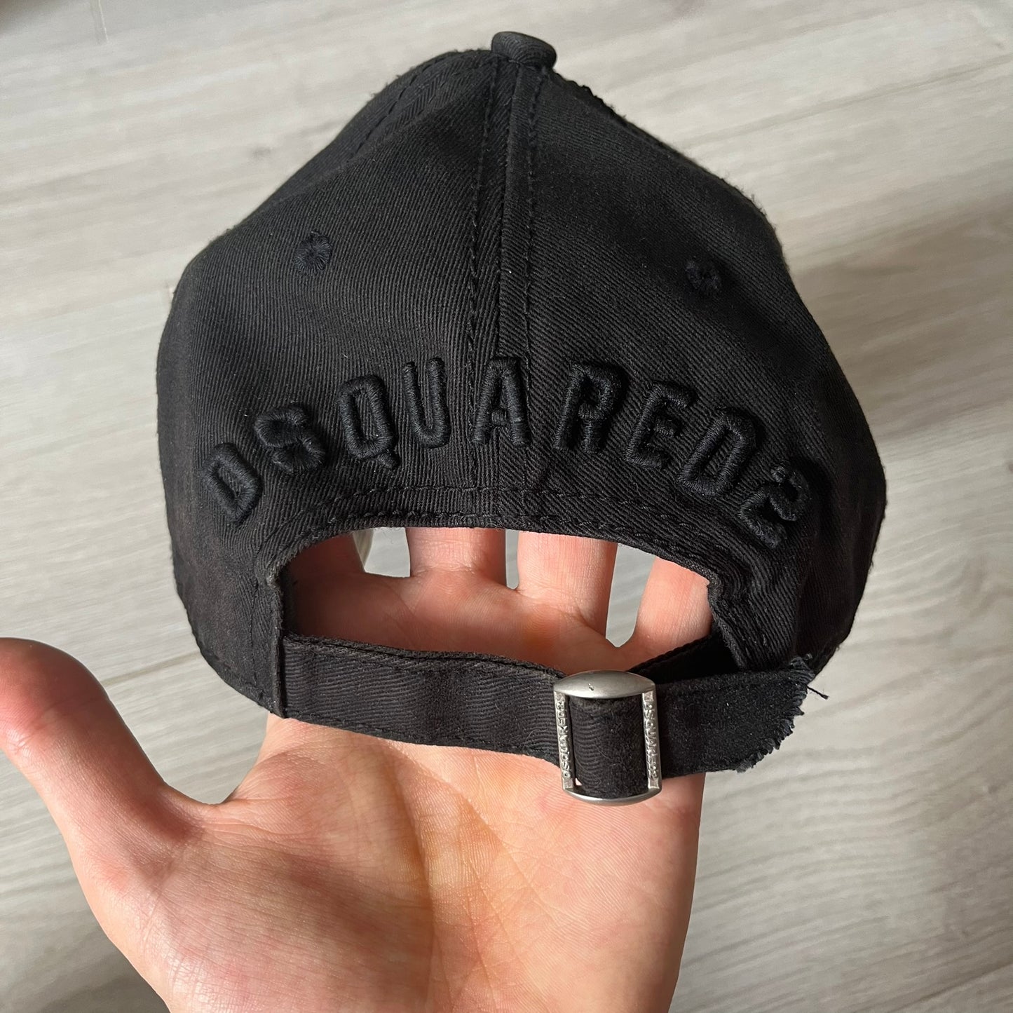 Black cap with 'Dsquared2' branding held by a hand on a light wooden surface