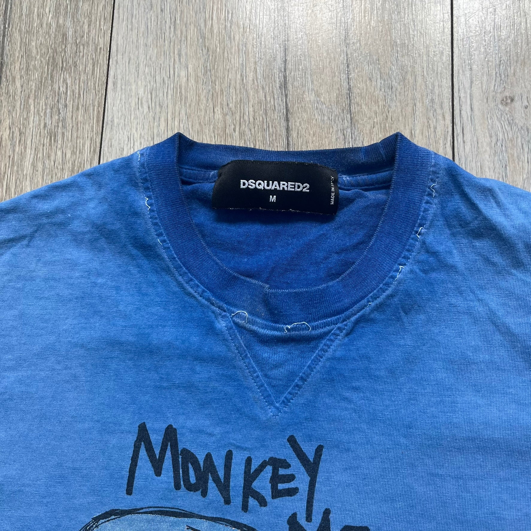 Dsquared2 Blue Rebel Monkey T-Shirt from the Spring/Summer 2015 collection. Crafted in Italy from cotton, the tee features a washed blue finish with darker tonal hems and a lighter faded center. The front displays a large stylized monkey graphic in black with light blue, with text reading “Monkey Me… Dsquared2 Motherfuc…” incorporated into the design.