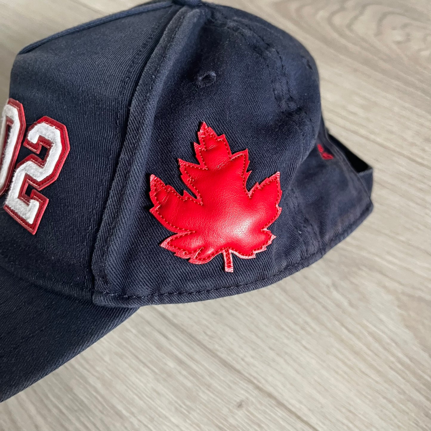 Navy blue cap with red maple leaf and white number 02 on a light gray surface