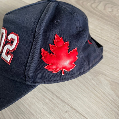 Navy blue cap with red maple leaf and white number 02 on a light gray surface