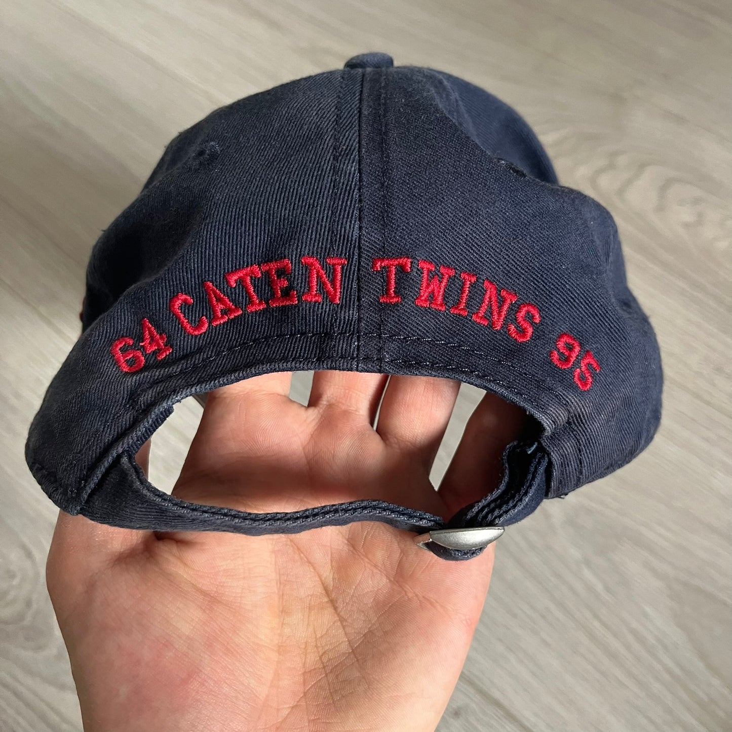 Navy blue cap with red text held in a hand on a neutral background