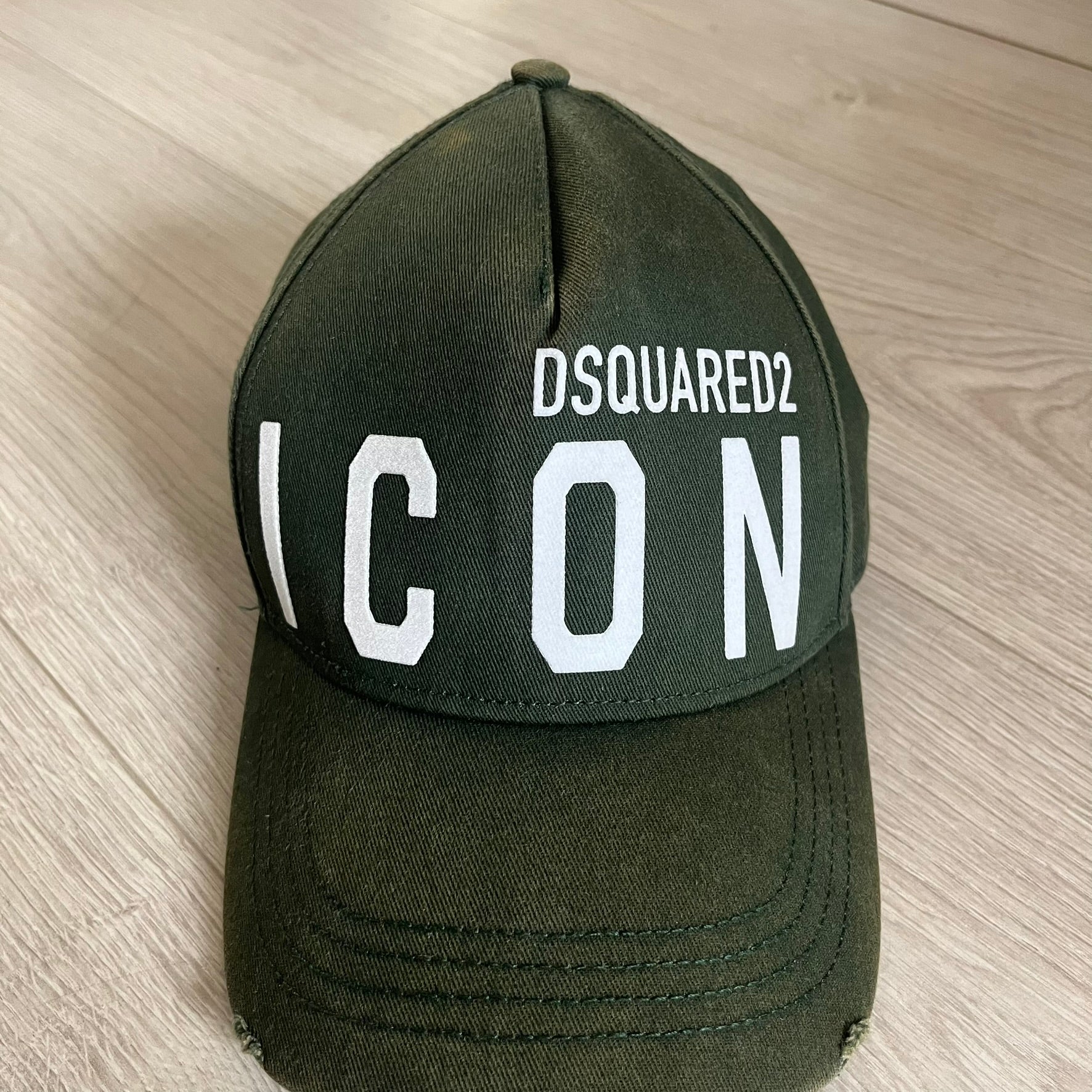 Green cap with 'DSQUARED2 ICON' text on a wooden surface