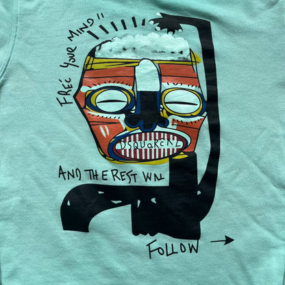Dsquared2 SS2015 “Free Your Mind” Crewneck is a turquoise cotton sweatshirt with a washed, faded finish and tonal variation across the fabric. The front features a black Basquiat-inspired figure with “Free Your Mind and the Rest Will Follow” text in a contrasting design. The piece is made in Italy and includes darker tonal hems with a lighter center fade for a worn effect.&nbsp;
