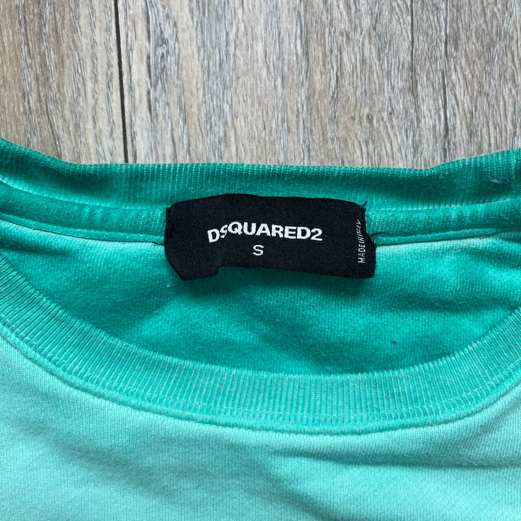 Dsquared2 SS2015 “Free Your Mind” Crewneck is a turquoise cotton sweatshirt with a washed, faded finish and tonal variation across the fabric. The front features a black Basquiat-inspired figure with “Free Your Mind and the Rest Will Follow” text in a contrasting design. The piece is made in Italy and includes darker tonal hems with a lighter center fade for a worn effect.&nbsp;