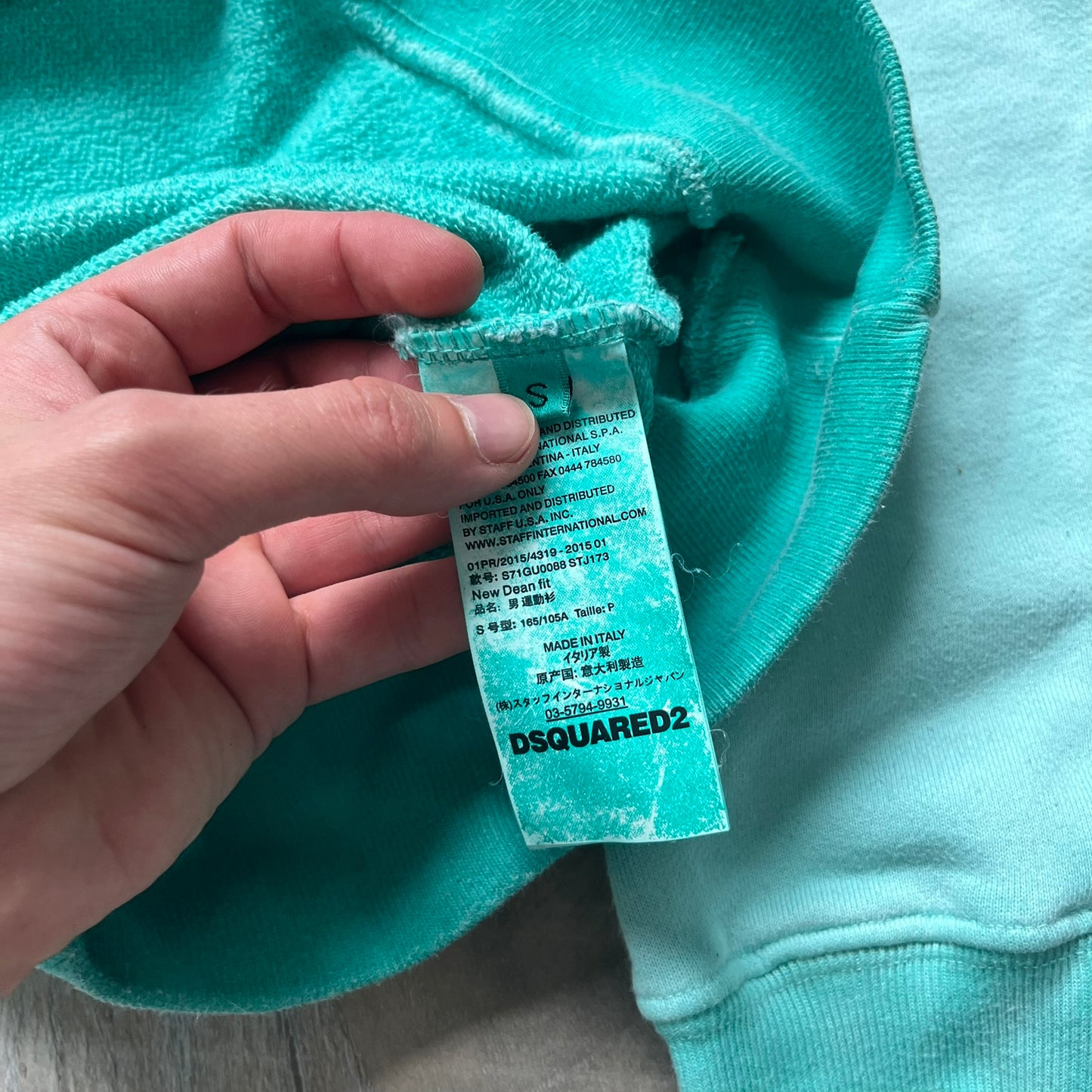 Dsquared2 SS2015 “Free Your Mind” Crewneck is a turquoise cotton sweatshirt with a washed, faded finish and tonal variation across the fabric. The front features a black Basquiat-inspired figure with “Free Your Mind and the Rest Will Follow” text in a contrasting design. The piece is made in Italy and includes darker tonal hems with a lighter center fade for a worn effect.&nbsp;